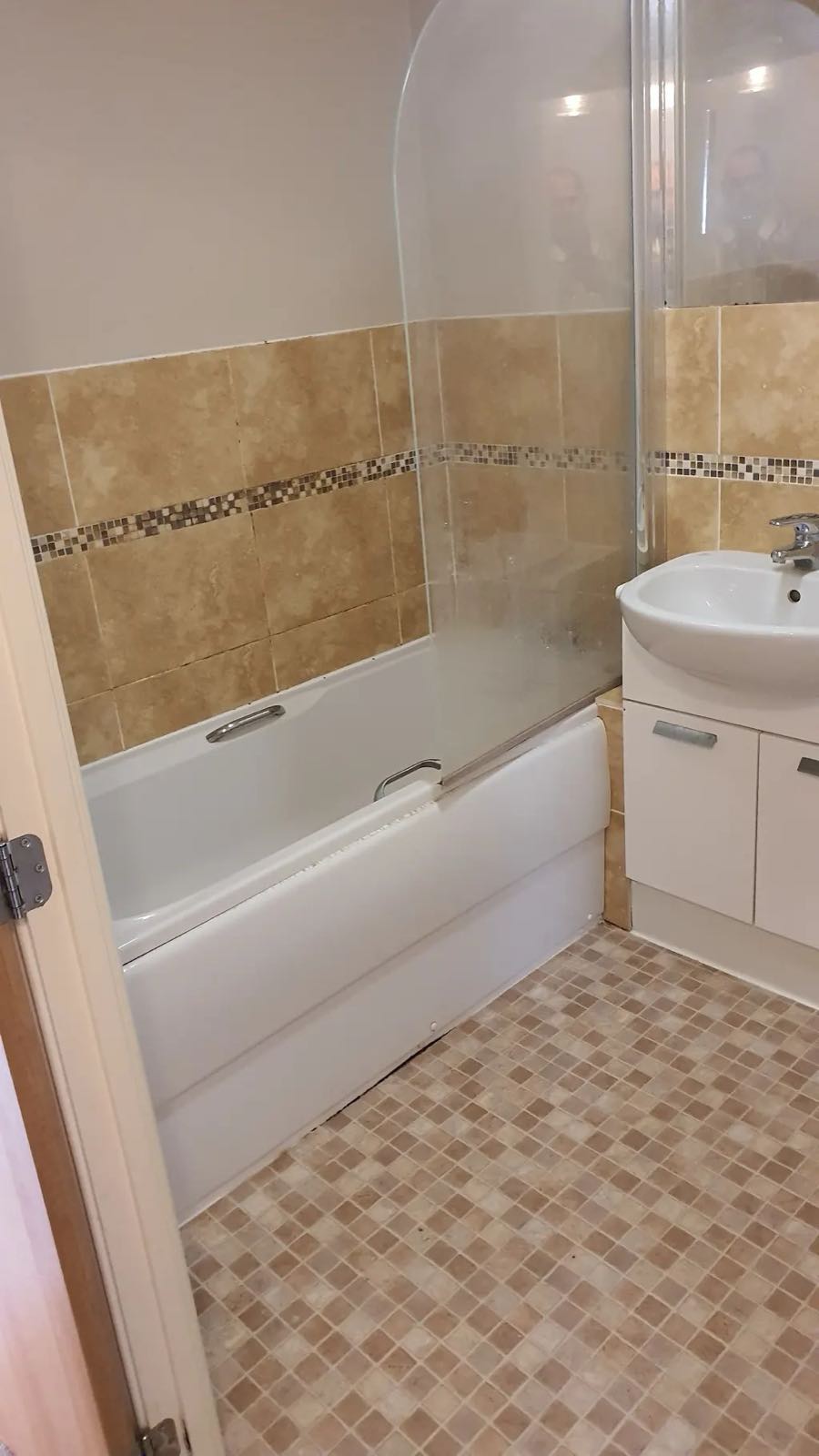 Before: the old bathroom with small mosaic wall tiles and a dated bath panel