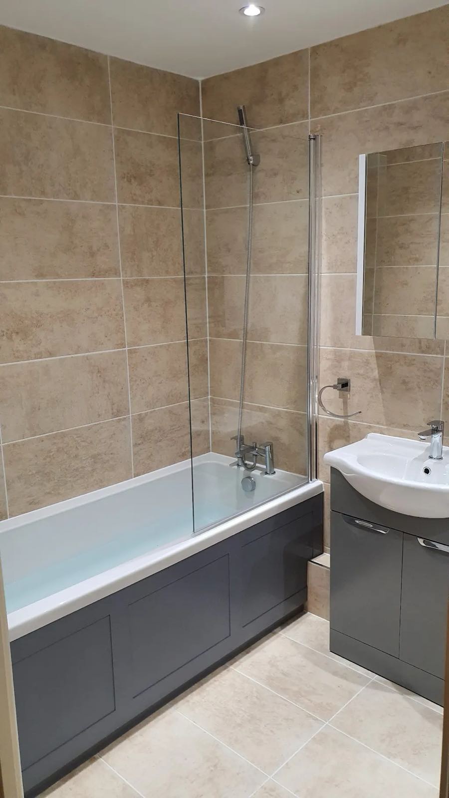 After: the same bathroom refitted with large stone-effect tiles, new bath, screen and grey vanity unit by ATR Kitchens and Bathrooms