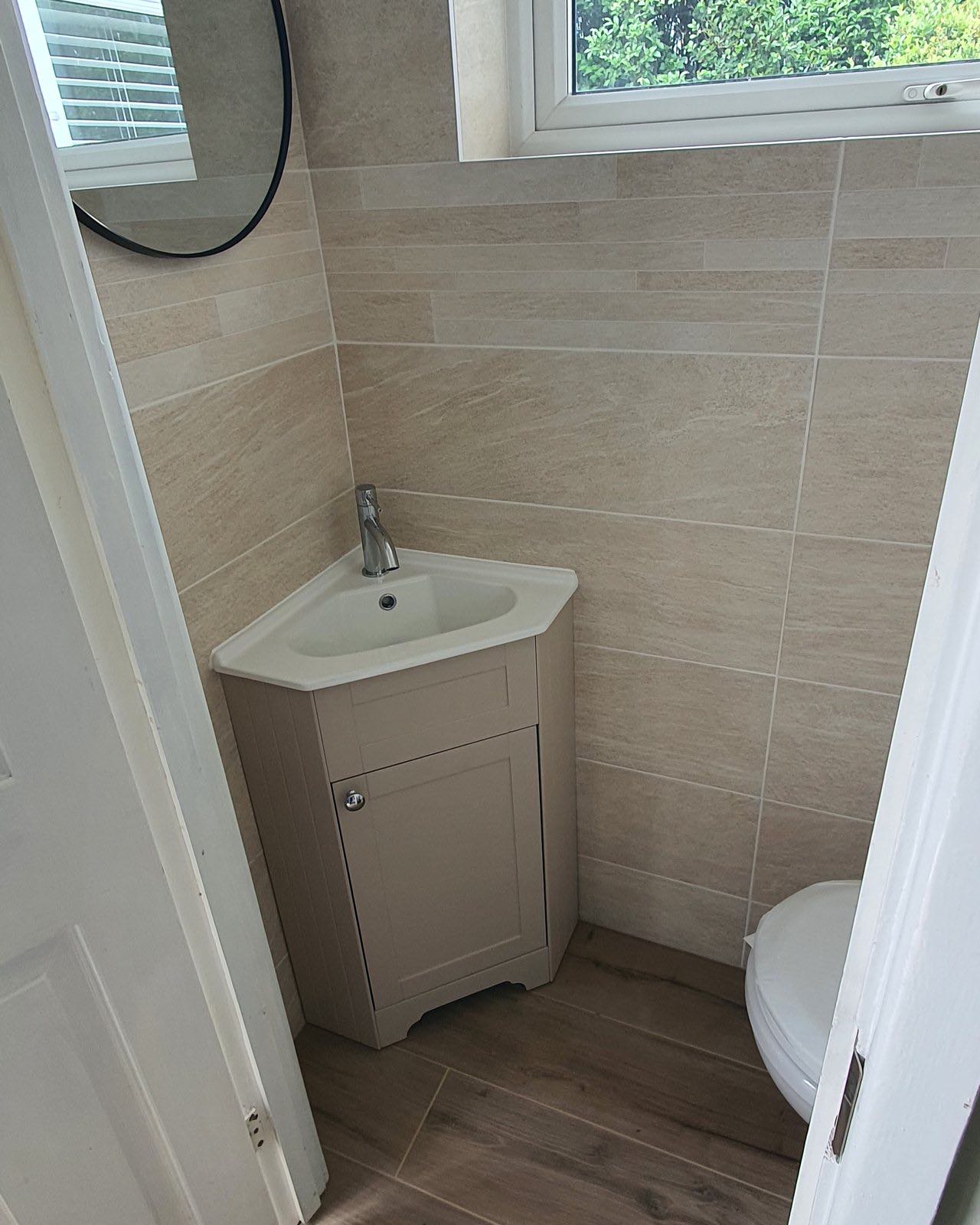 After: the finished cloakroom with a corner vanity unit, large-format tiles and wood-effect floor by ATR Kitchens and Bathrooms