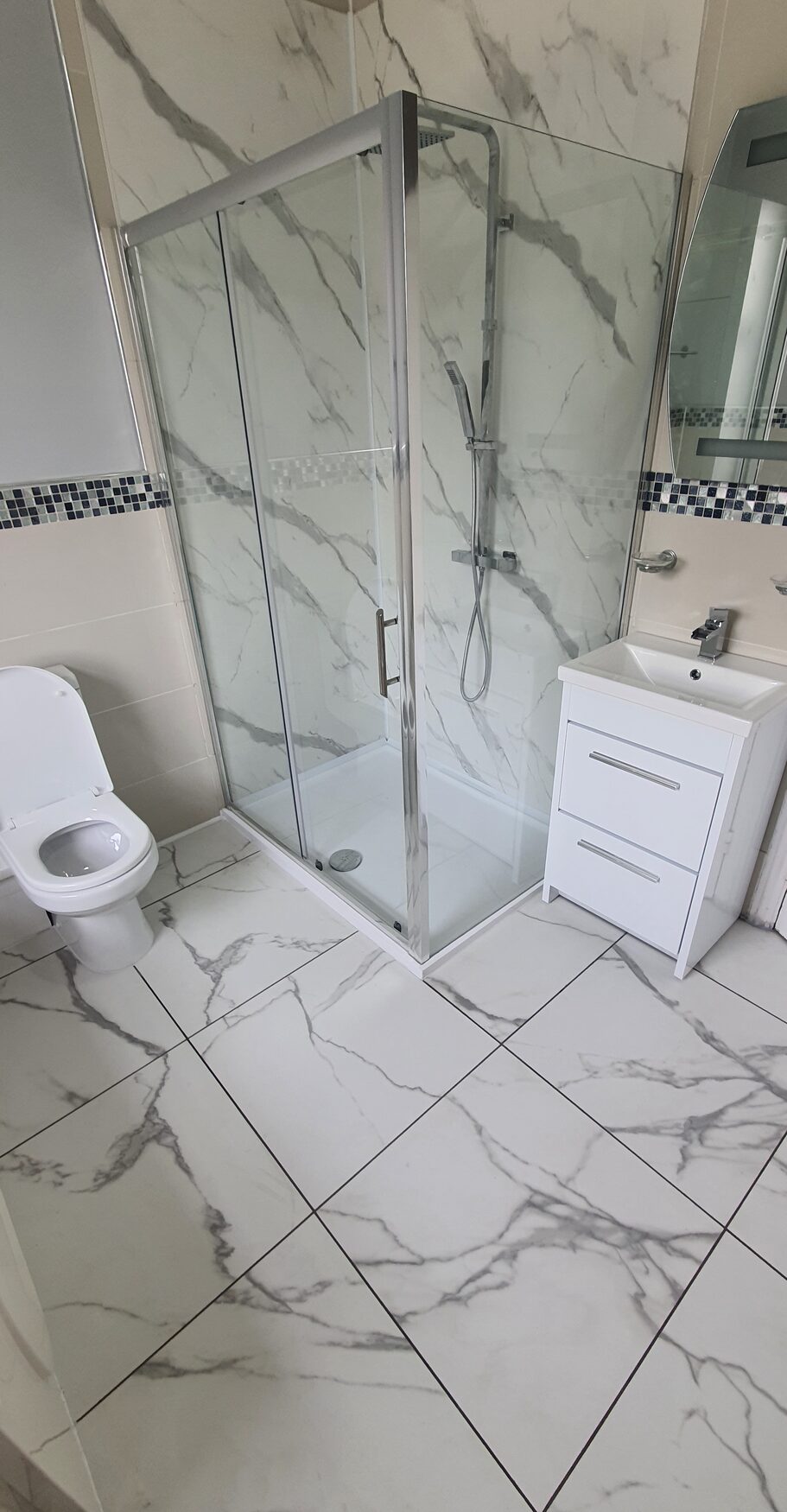 Insurance repair bathroom finished in marble-effect tiles with a corner shower enclosure by ATR Kitchens and Bathrooms in Grays