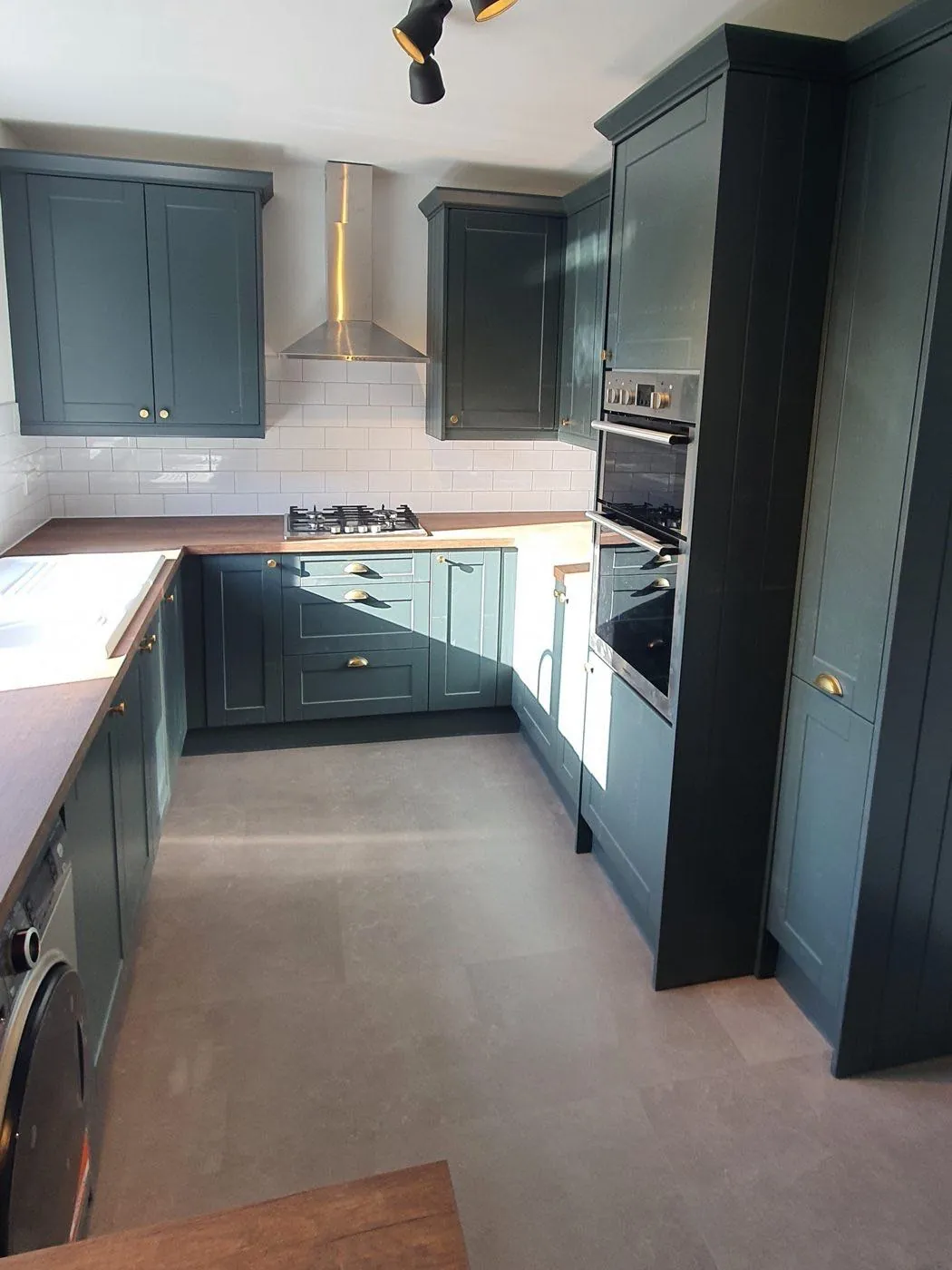 Dark green shaker-style kitchen with built-in ovens, a chimney extractor hood and tiled splashback